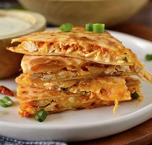 A close up side view of buffalo chicken quesadillas on a white plate.