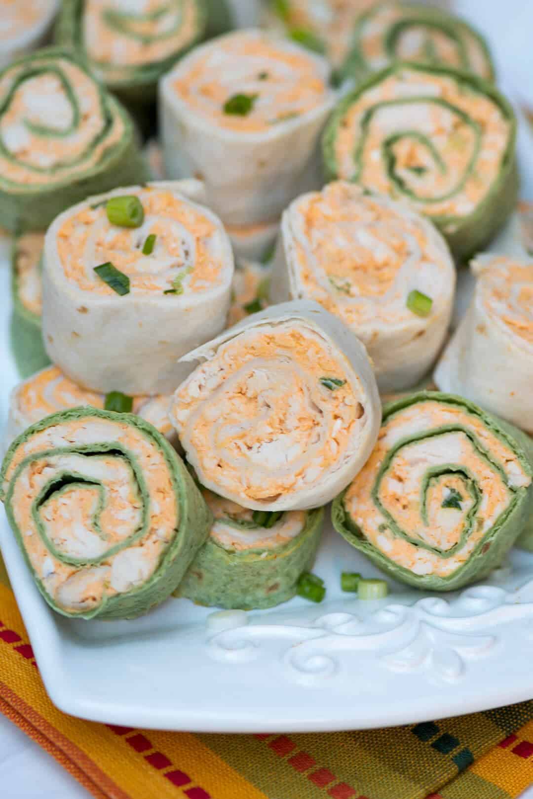 A close up view of many buffalo chicken tortilla pinwheels stacked on a white plate.