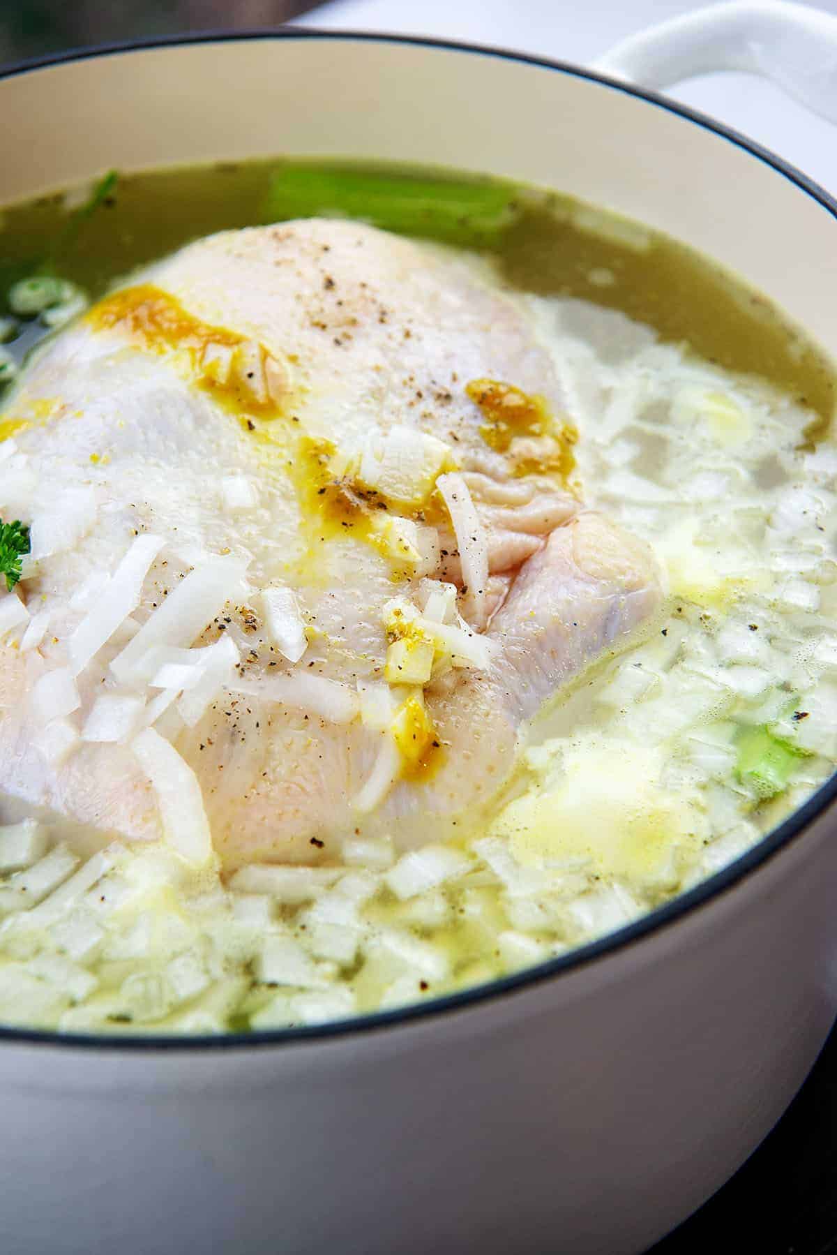 whole chicken in pot with vegetables to make stock.