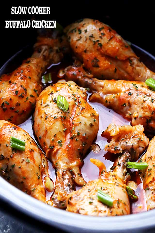 Cooked buffalo chicken flavored drumsticks resting in a slow cooker.