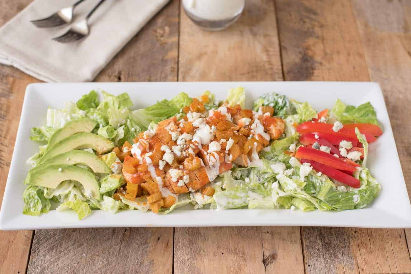 Warm buffalo chicken salad on a white plate resting on a wooden table.