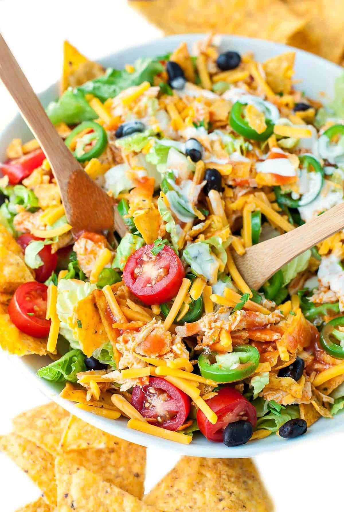 A top down view of a white bowl of buffalo chicken taco salad next to corn chips.