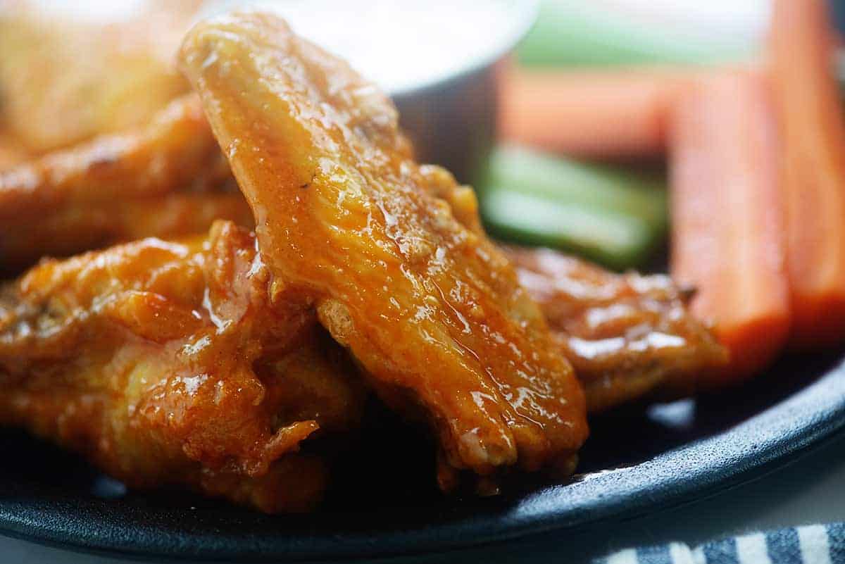 Close up of crispy air fried chicken wings on a plate next to celery and carrots.