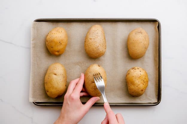 a woman poking holes in potatoes with a fork.