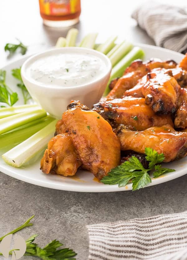 Instant pot honey buffalo chicken wings on a white plate next to celery sticks and a bowl of ranch dip.