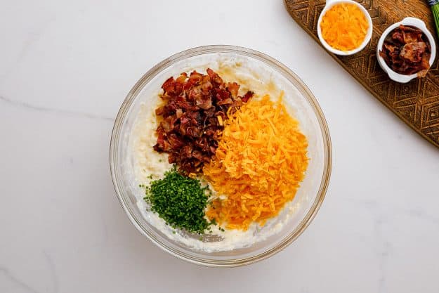 mashed potatoes with cheddar, bacon, and chives in a glass bowl.