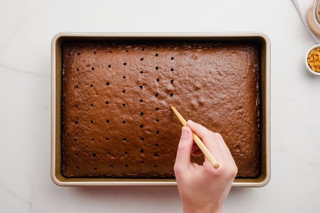 a woman using a skewer to poke holes in a chocolate cake.