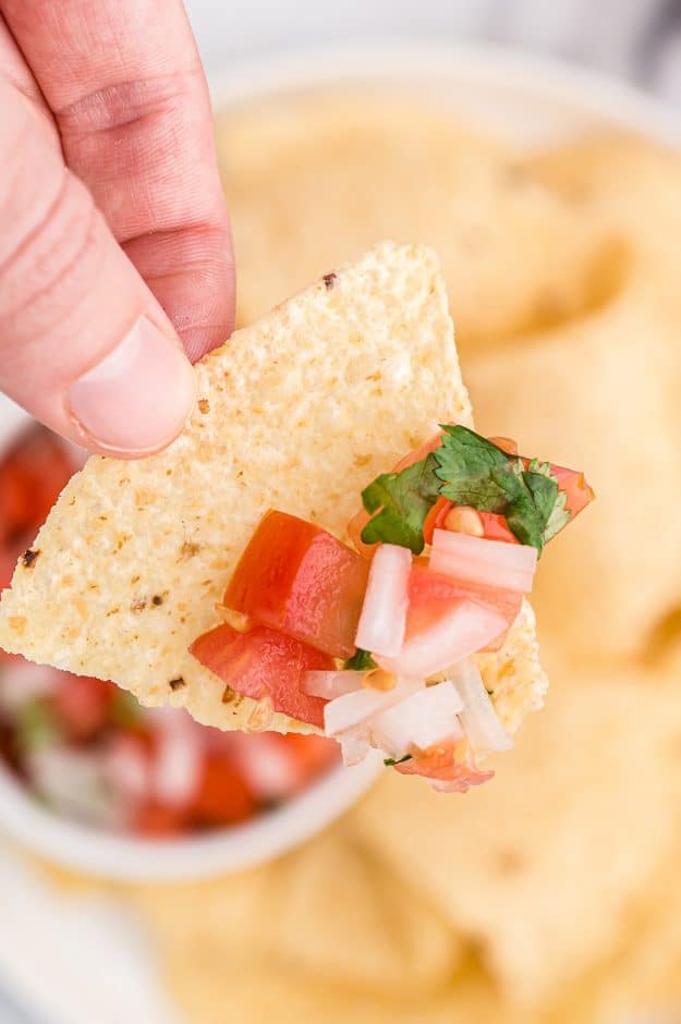 woman's hand holding a chip with pico de gallo on it.
