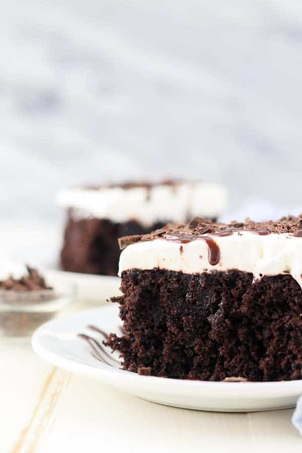 A close up side view of two slices of homemade chocolate poke cake on separate white plates.