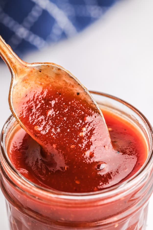 bourbon bbq sauce dripping off a spoon into a mason jar.