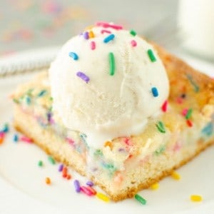 A close up side view of a slice of funfetti butter cake topped with a scoop of ice cream and sprinkles.