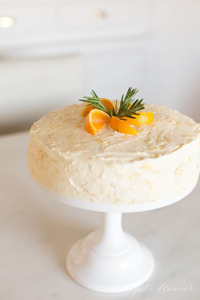 A mandarin orange cake on a serving platter with fresh sliced oranges on top.