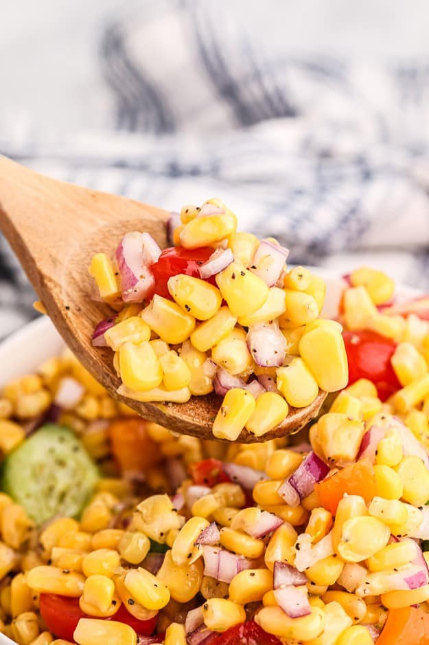corn salad on wooden spoon over white bowl.