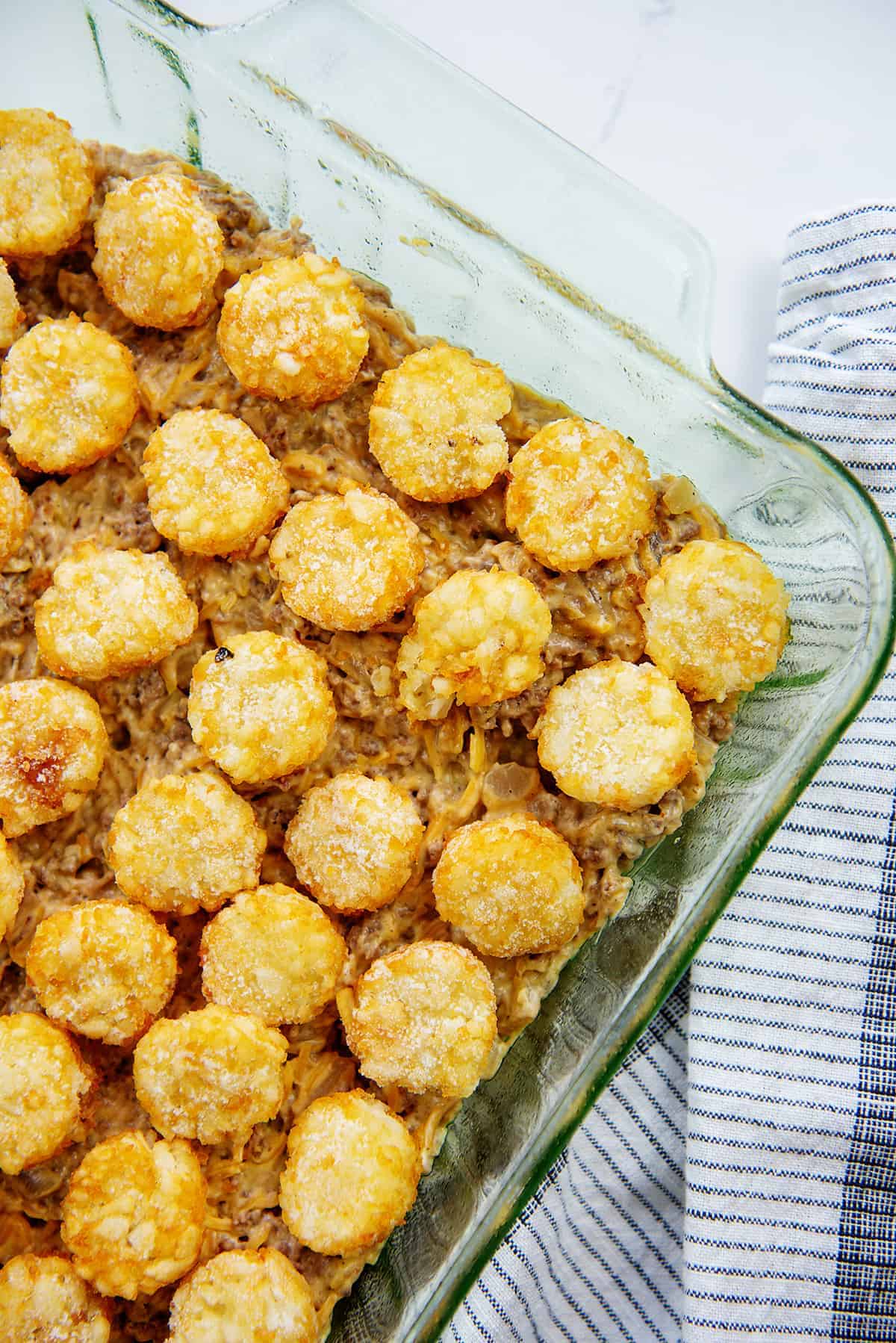 cheeseburger casserole topped with tater tots in glass baking dish.