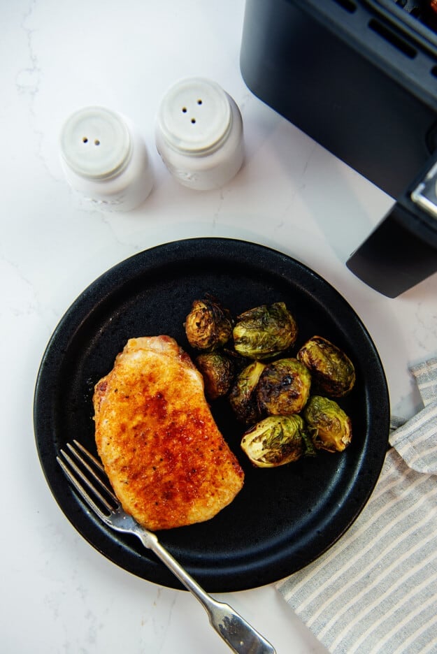 overhead view of pork chop and Brussels sprouts on black plate.