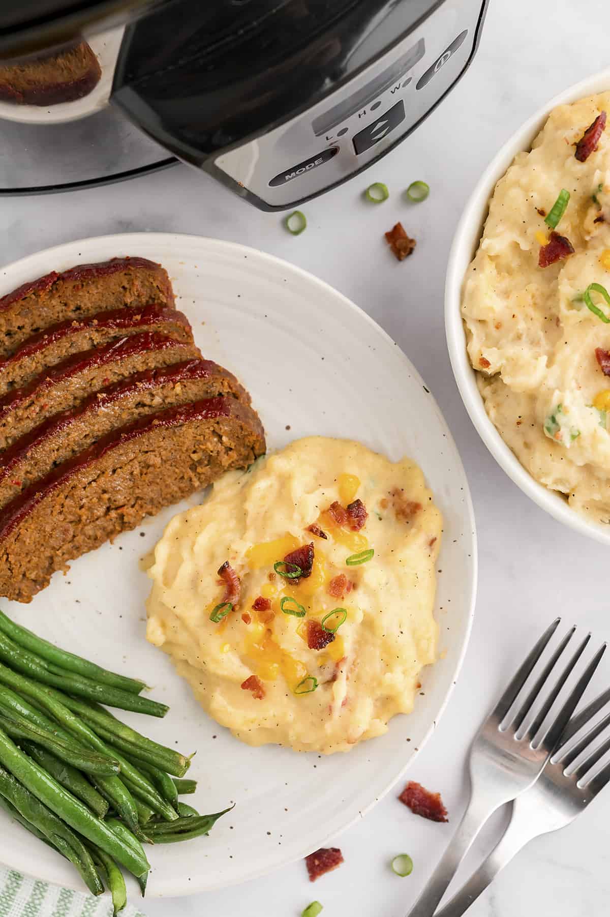 Loaded mashed potatoes on plate with meatloaf and green beans.