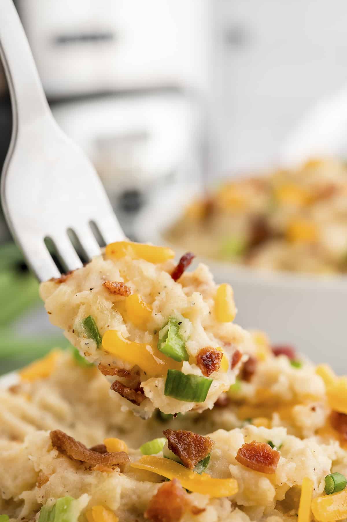 Forkful of loaded mashed potatoes with bacon, cheddar, and green onion.