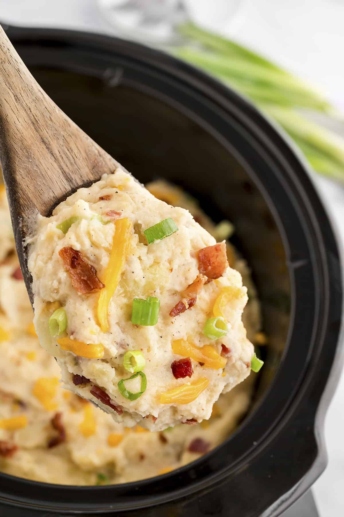 Loaded mashed potatoes on wooden spoon.