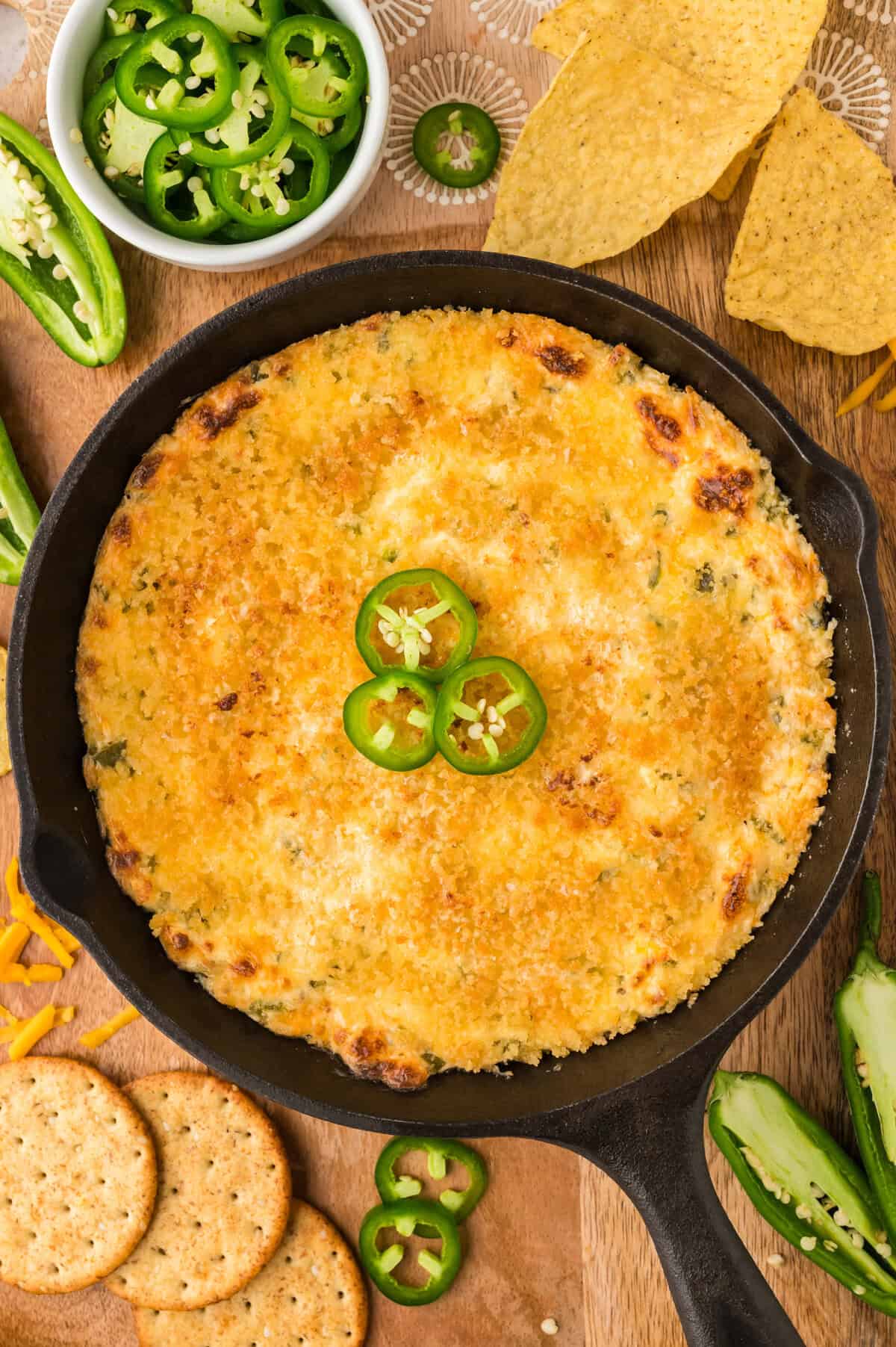 Jalapeno popper dip in cast iron skillet surrounded by crackers and chips.