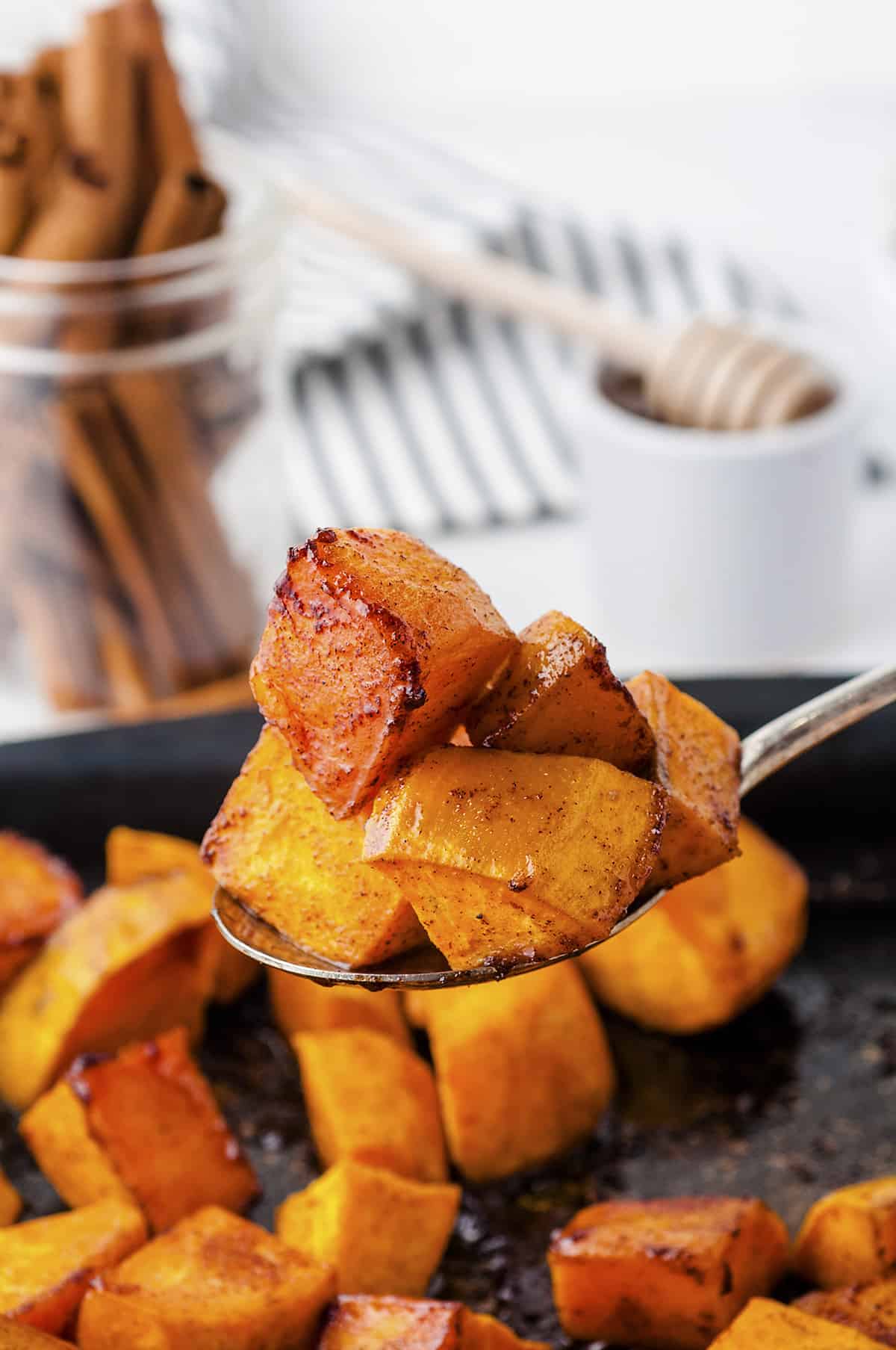 Oven roasted sweet potatoes on spoon over pan.
