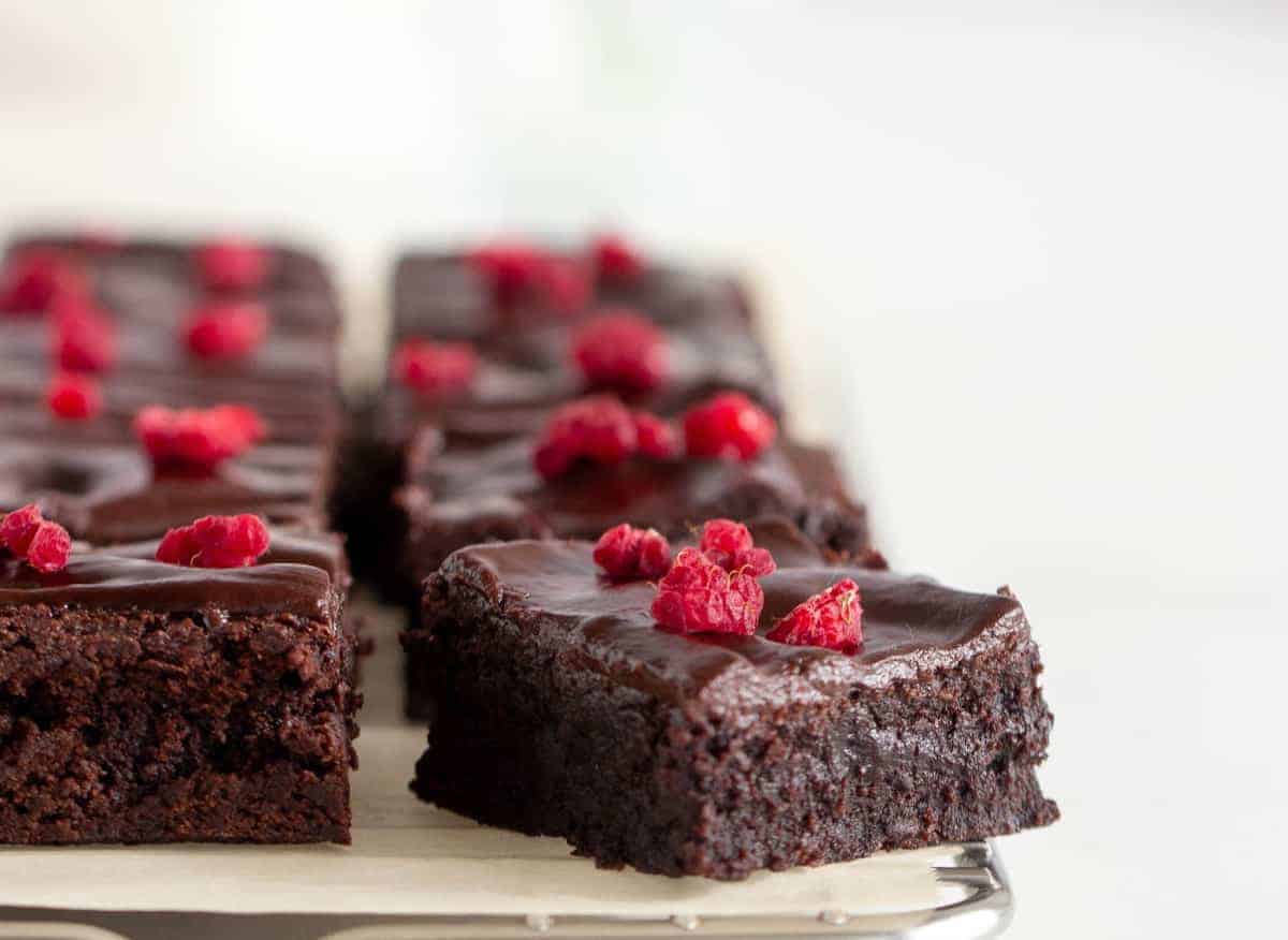 A close up side view of sliced cocoa topped with fresh raspberry resting on a parchment lined baking sheet.
