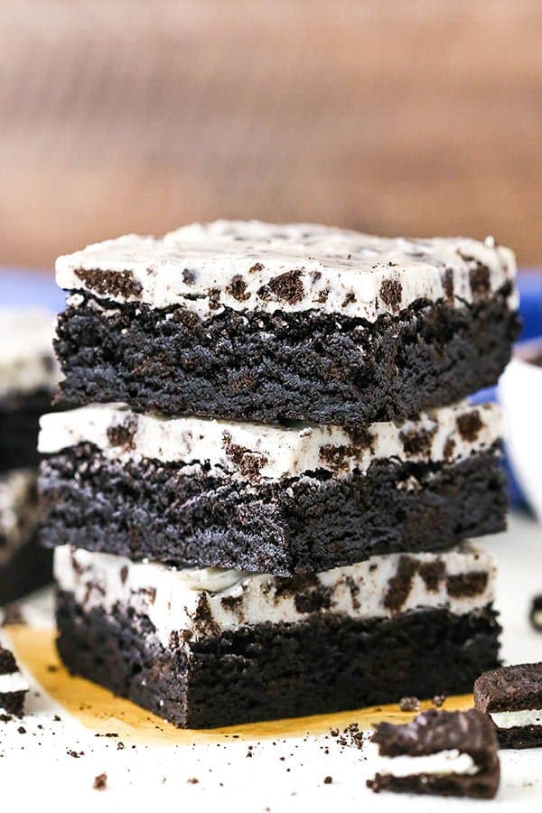 A close up side view of three stacked cookies and cream Oreo brownies next to crushed Oreo cookies.