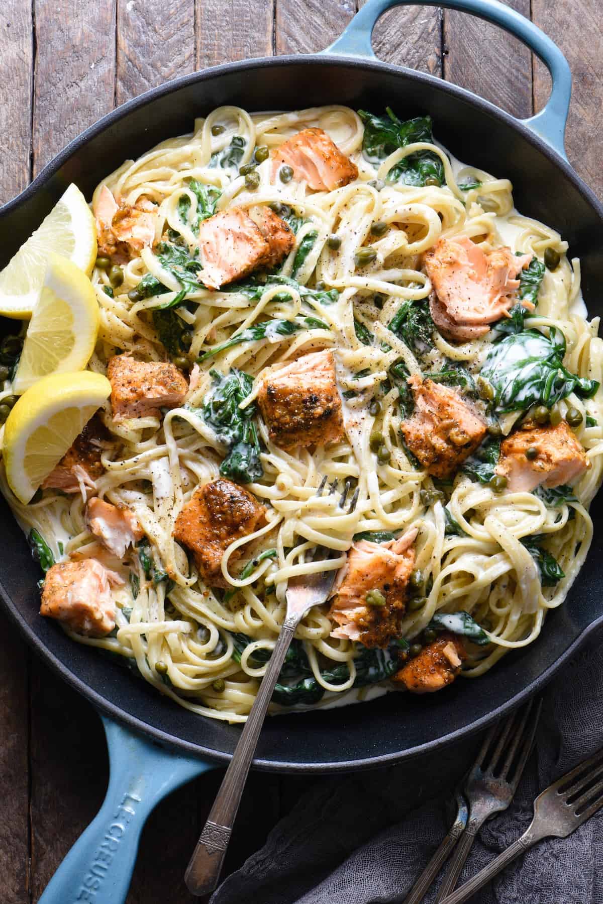 A top down view of creamy salmon pasta with spinach in a cast iron skillet on a wooden table.