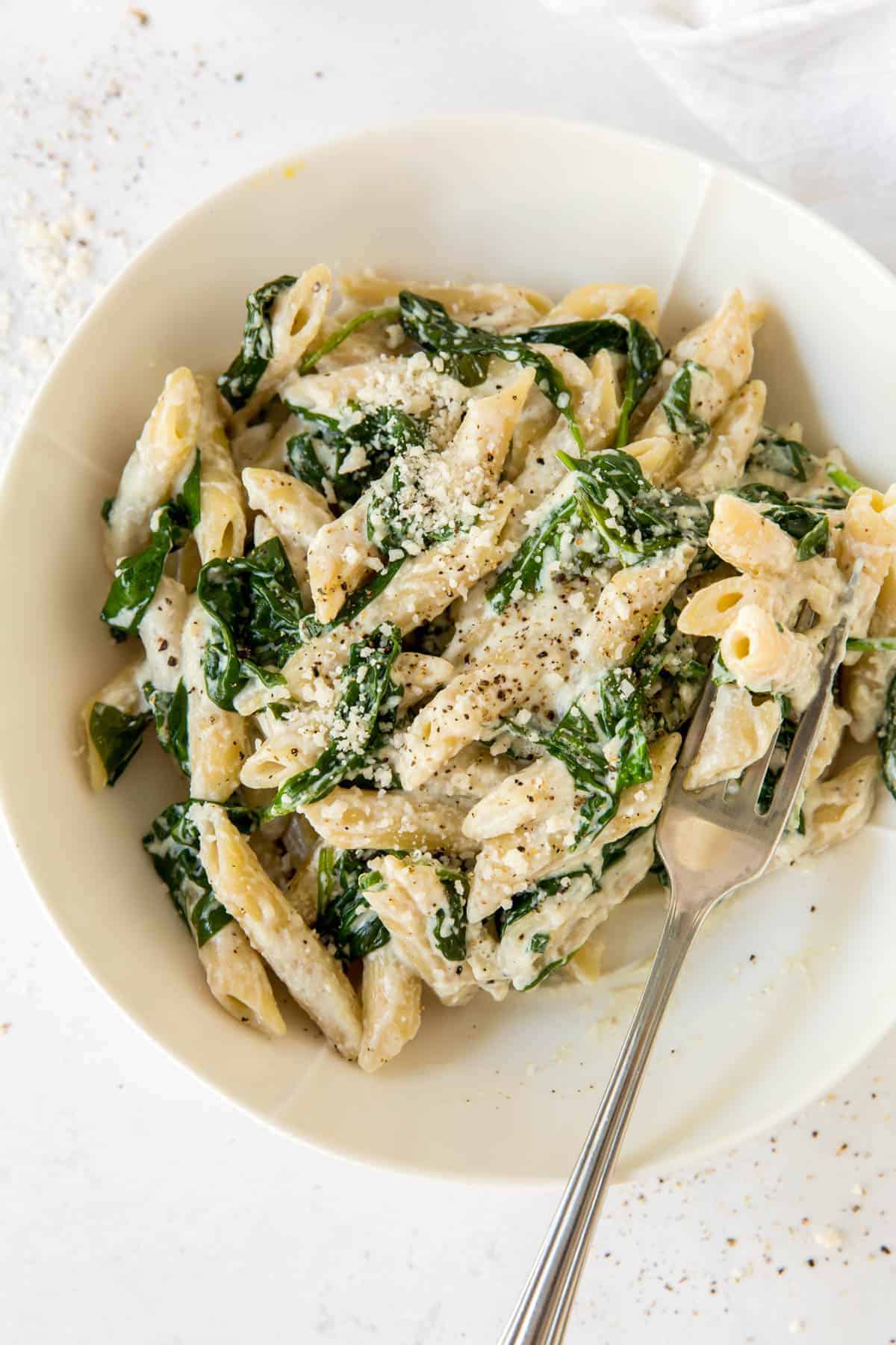 A top down view of spinach ricotta pasta on a white plate with a fork.