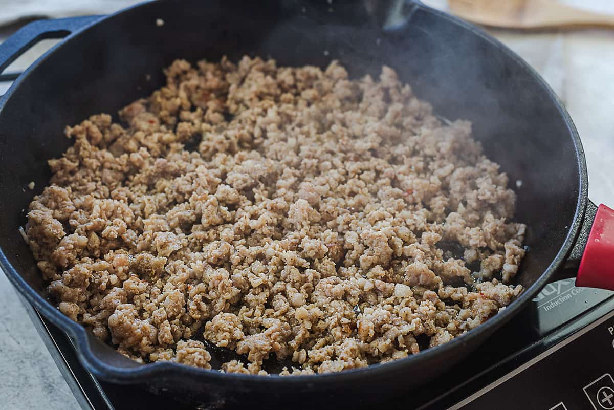 Ground sausage being cooked in a cast iron skillet.