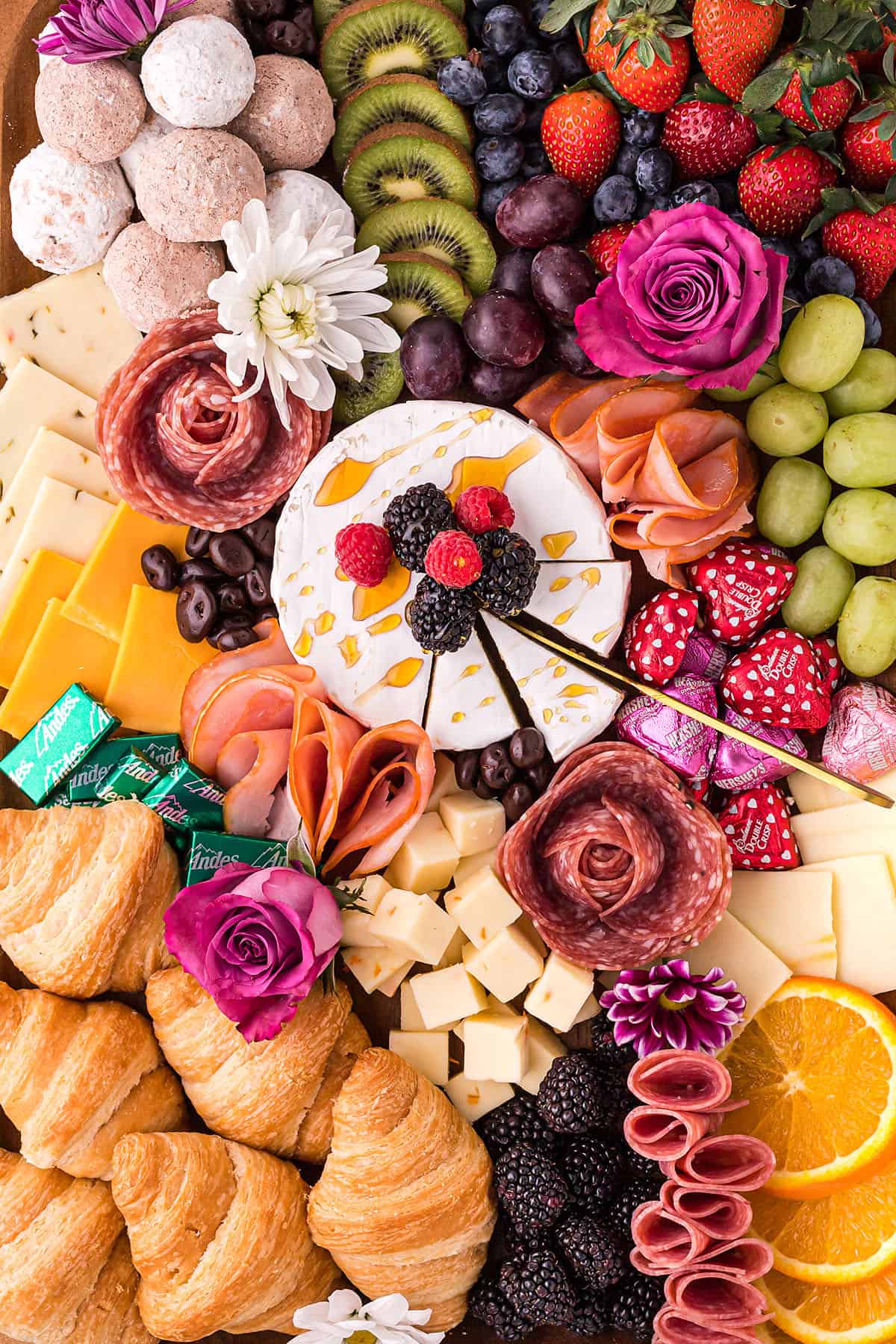charcuterie board with cheese, meat, fruit, and flowers.