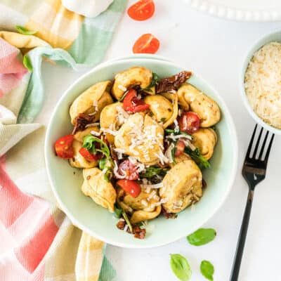 tortellini pasta salad in bowl surrounded by tomatoes and basil.