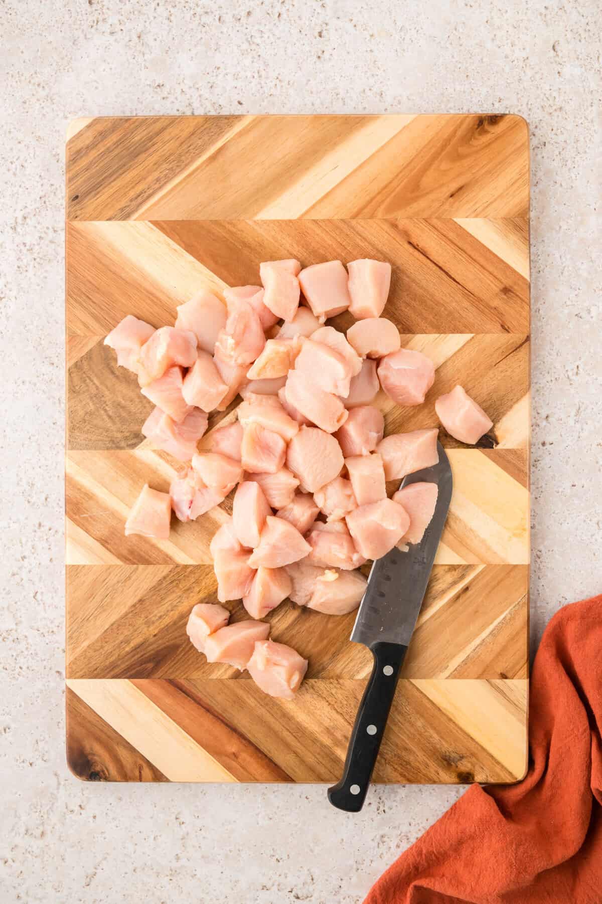 Chopped chicken breasts on wooden cutting board.