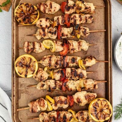 Greek chicken skewers on baking sheet.