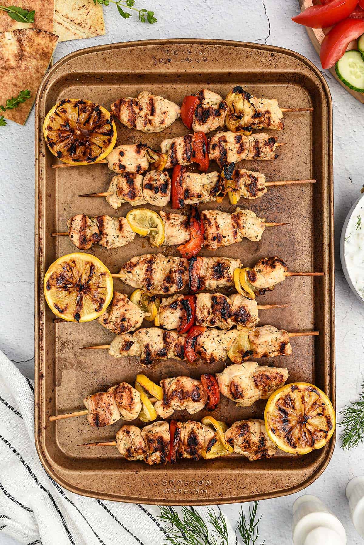 Greek chicken skewers on baking sheet.