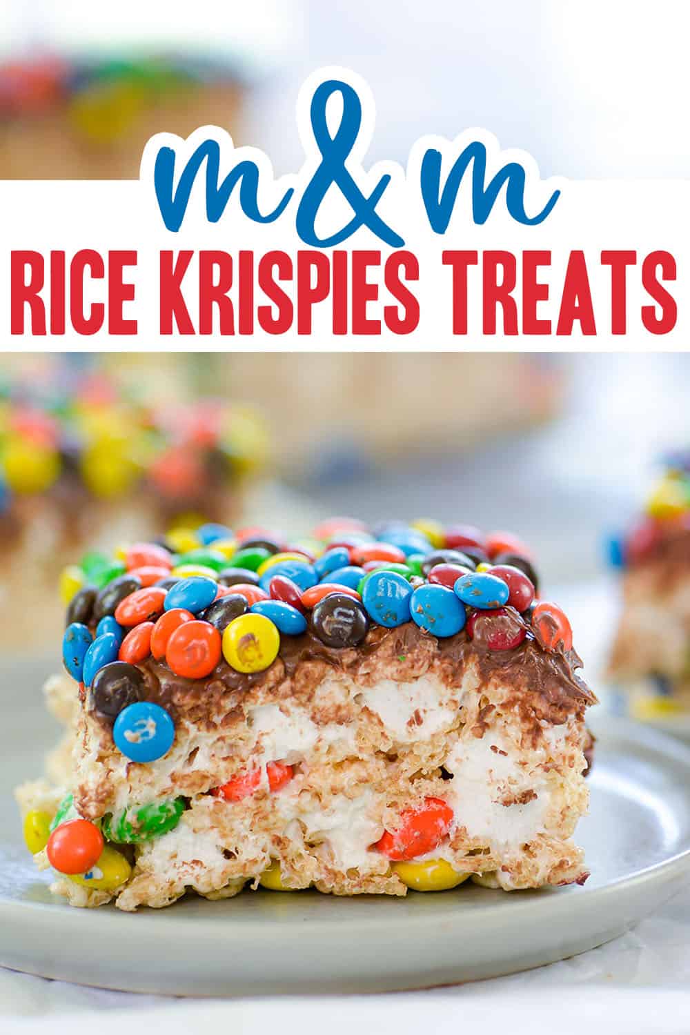 thick rice krispies treat topped with chocolate and m&m's on white plate.