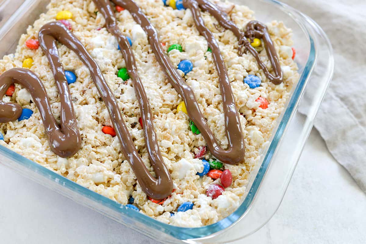 chocolate drizzled over the top of rice krispies treats in glass pan.