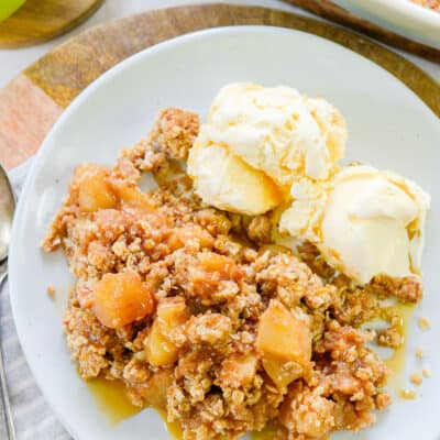 apple crumble recipe on white plate with 2 scoops of vanilla icec cream.