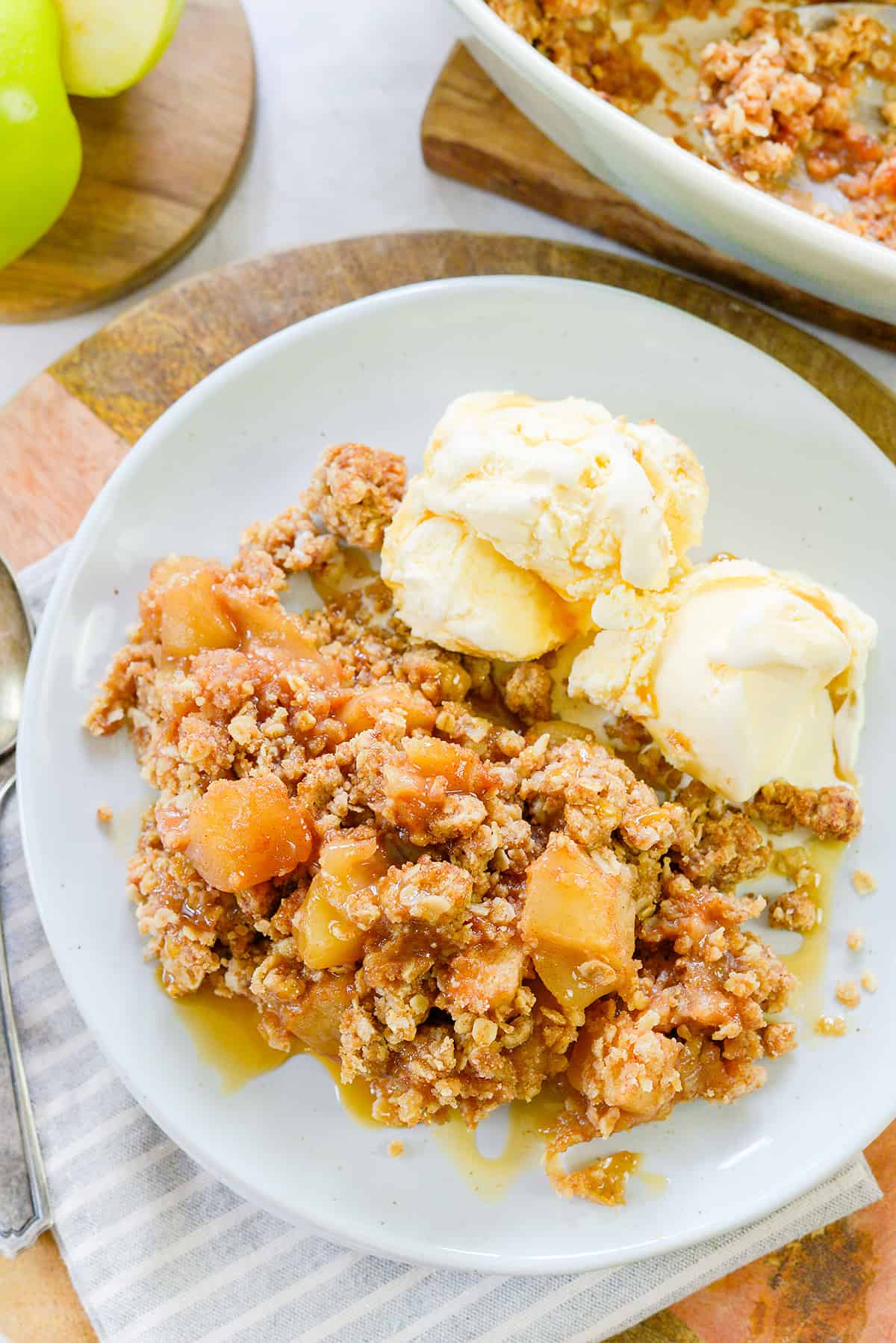 apple crumble recipe on white plate with 2 scoops of vanilla icec cream.