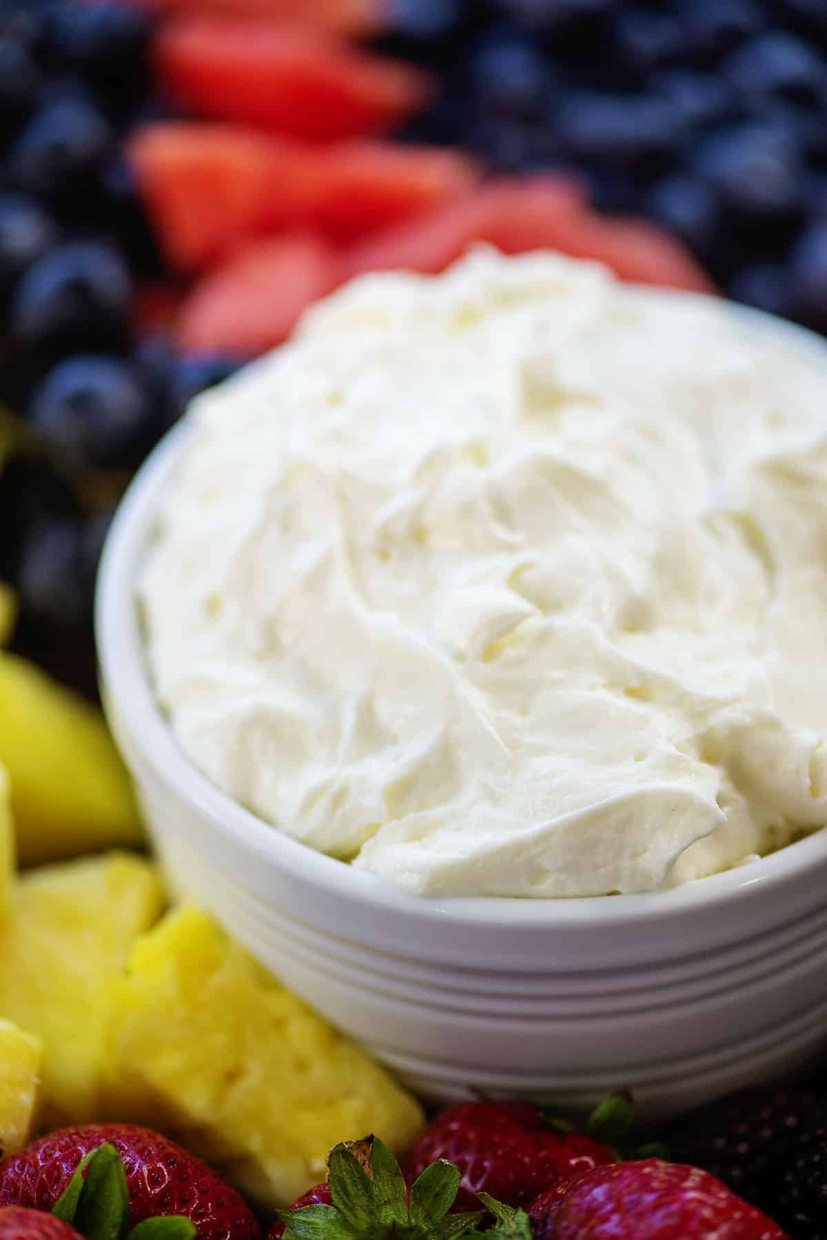 bowlful of cream cheese fruit dip surrounded by fruit.