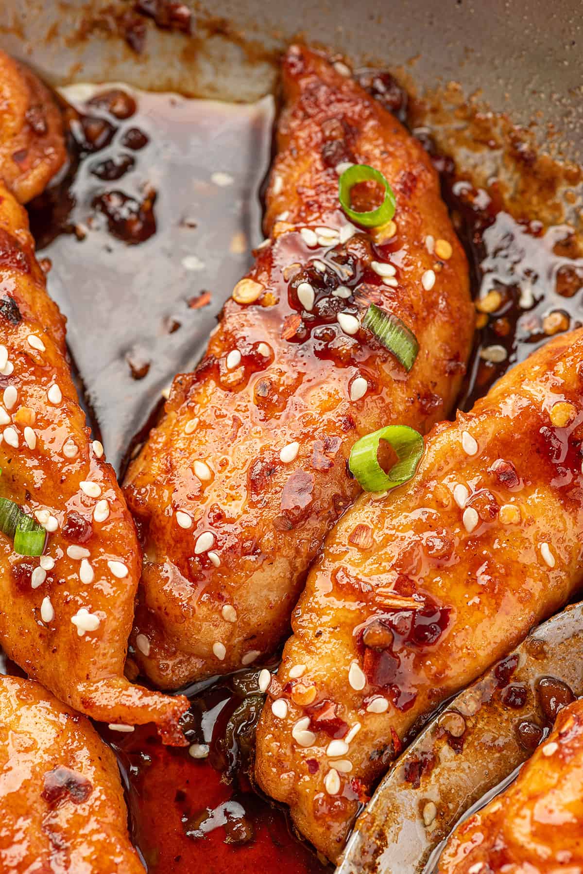 Honey garlic chicken tenders in skillet, coated in sauce.