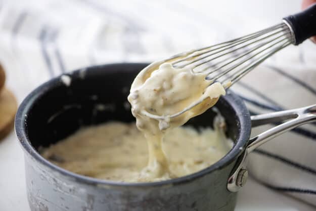 Whisk with cream of mushroom soup dripping off it into a pan.