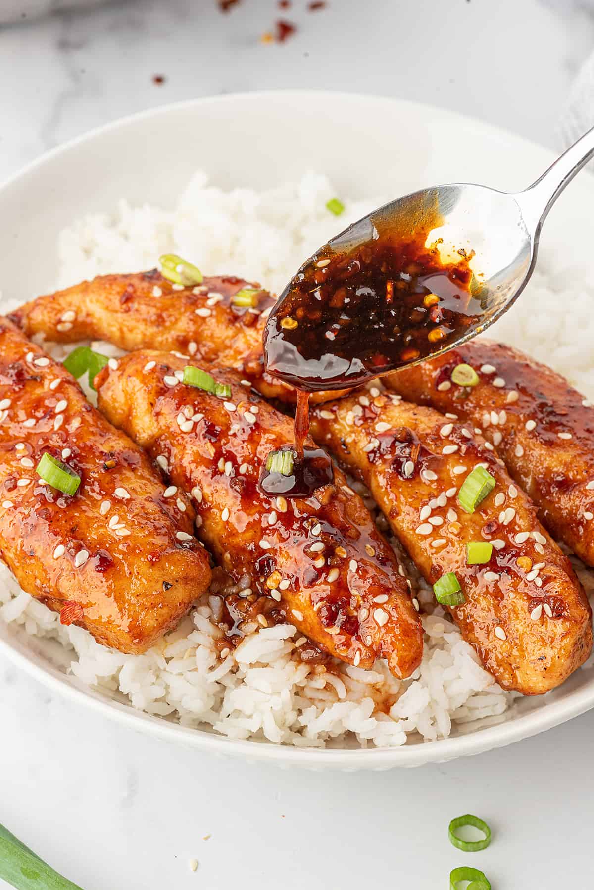 Honey garlic sauce being spooned over chicken.