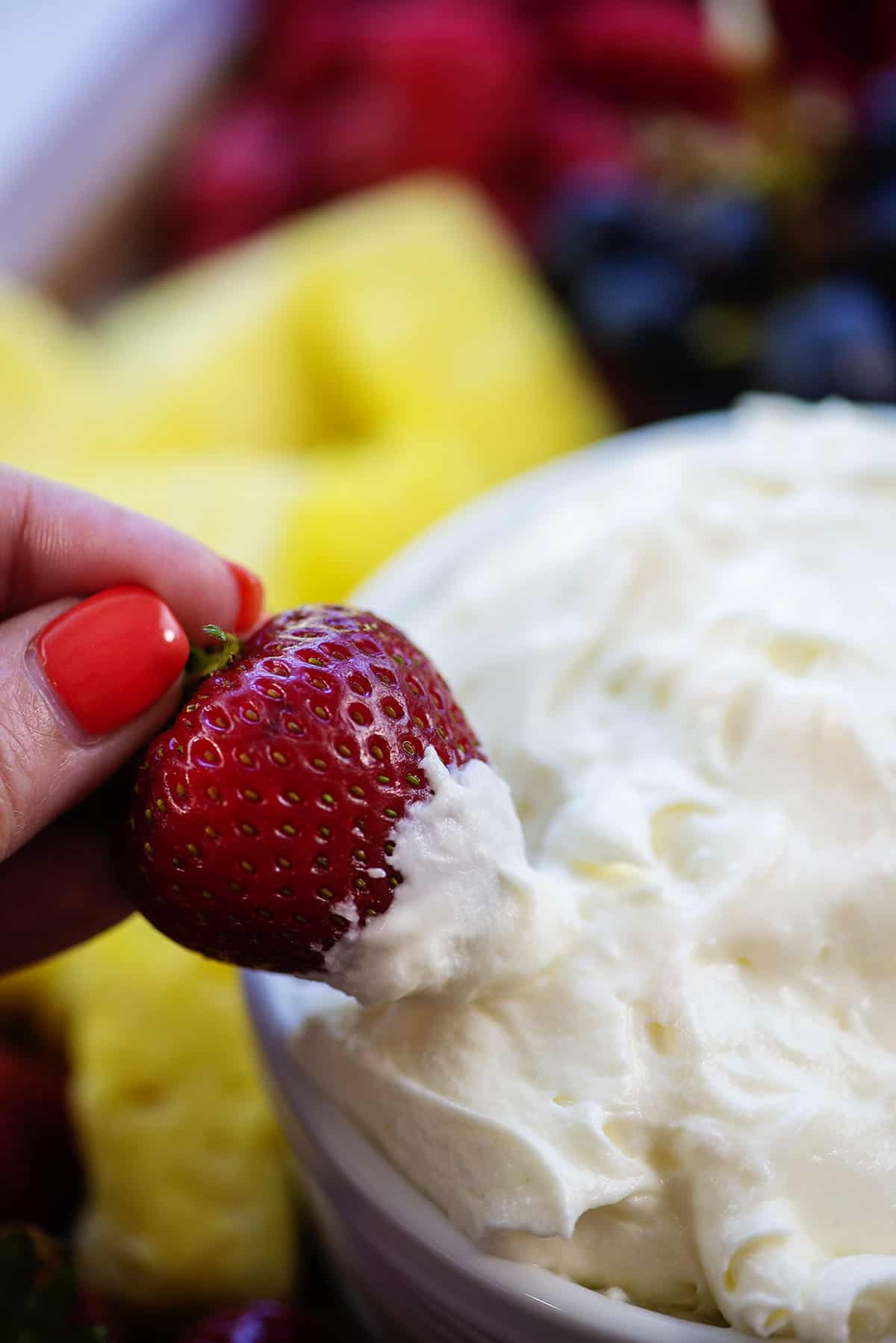 woman's hand dipping a strawberry in fruit dip.