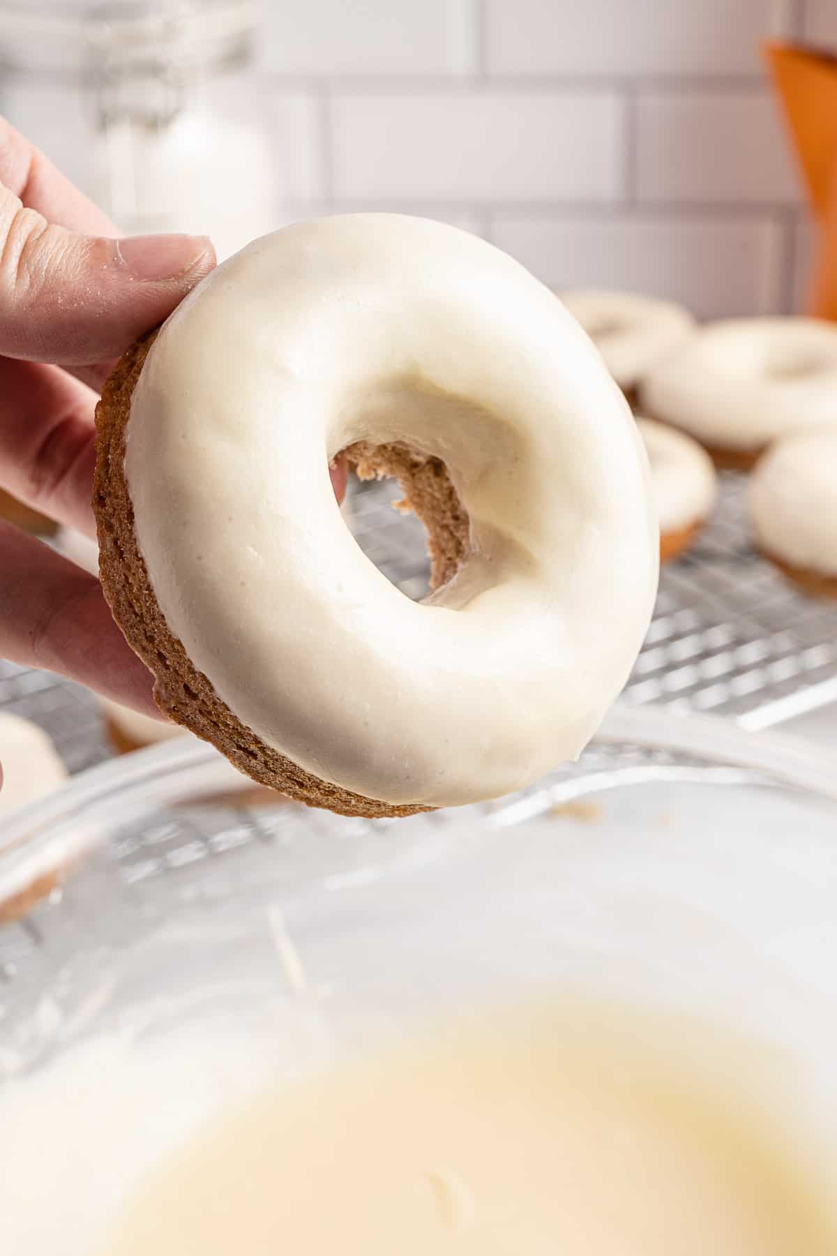 hand holding a glazed donut over bowl of glaze.