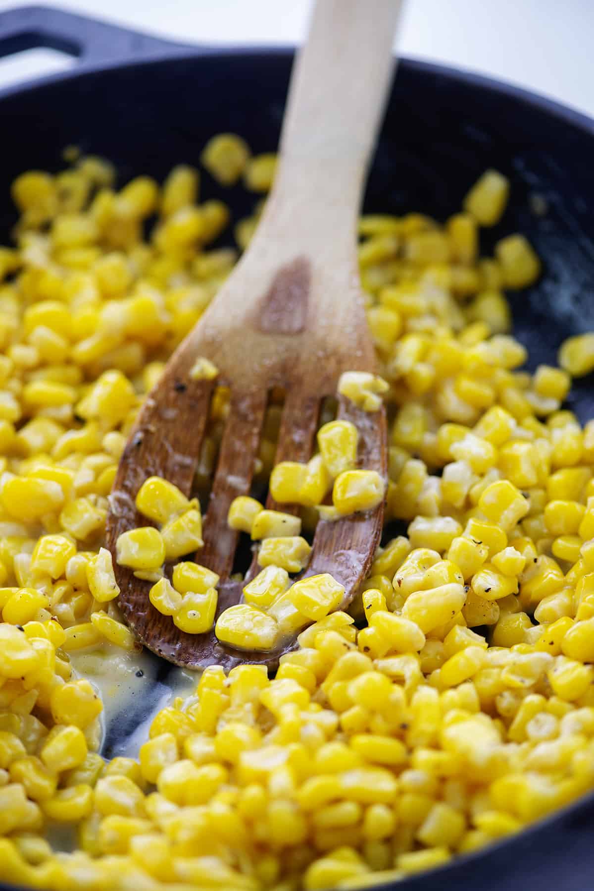 Wooden spoon in pan full of honey butter skillet corn.