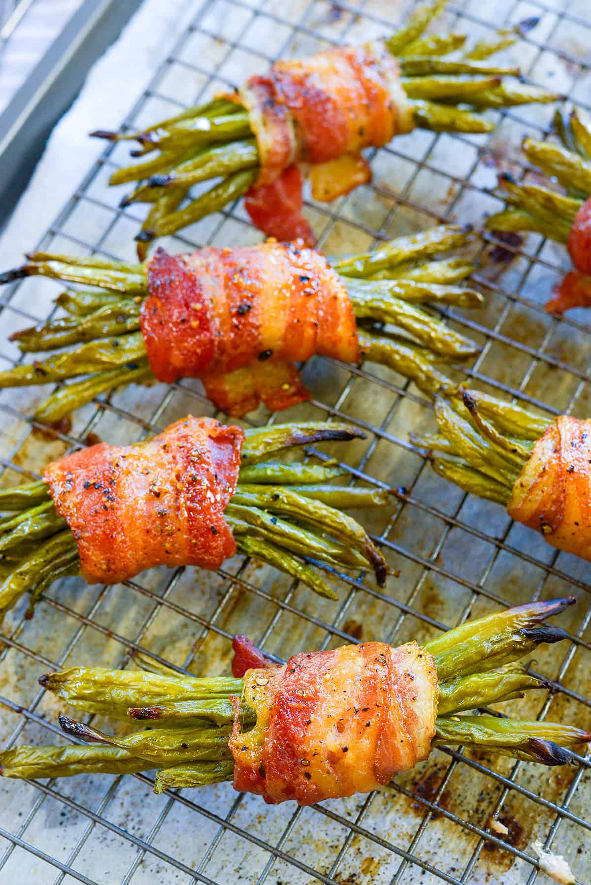 Roasted green bean bundles wrapped in bacon on baking sheet.