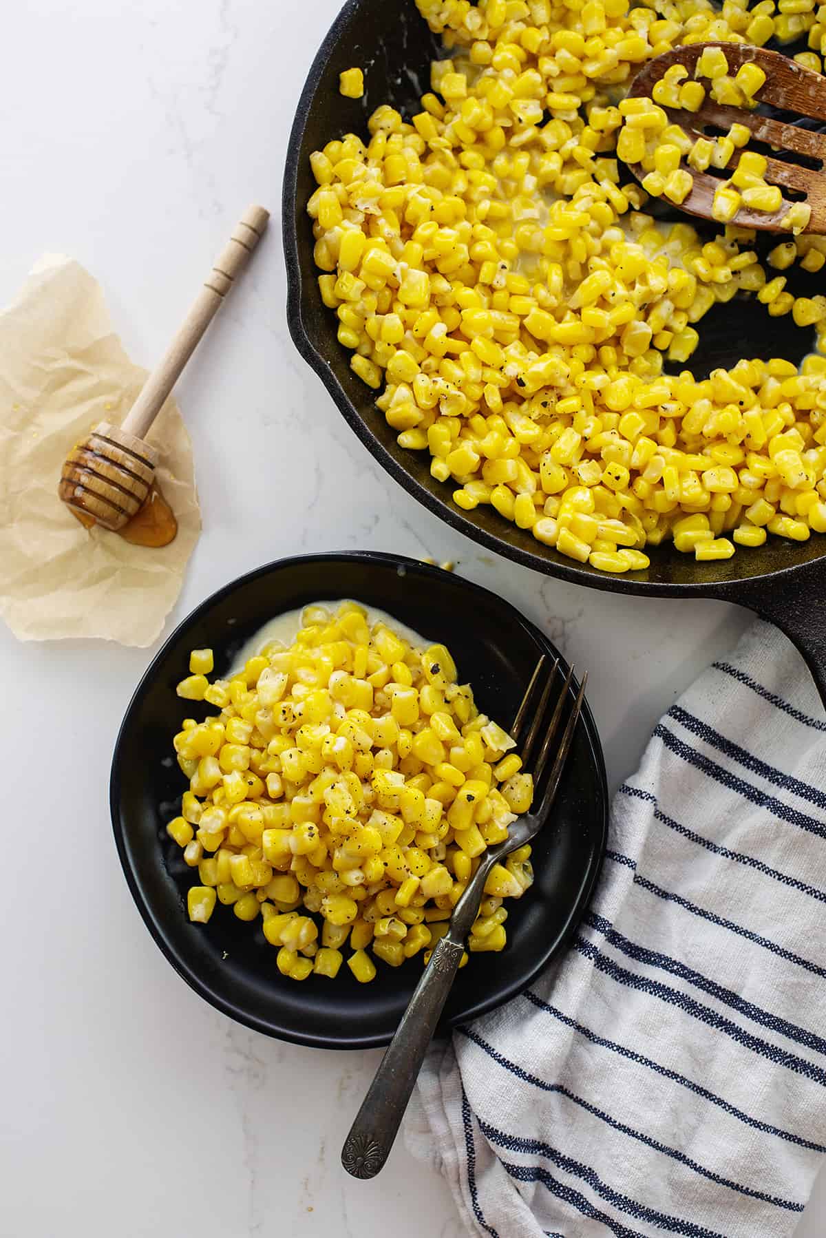 Honey butter skillet corn on black plate next to honey dipper.