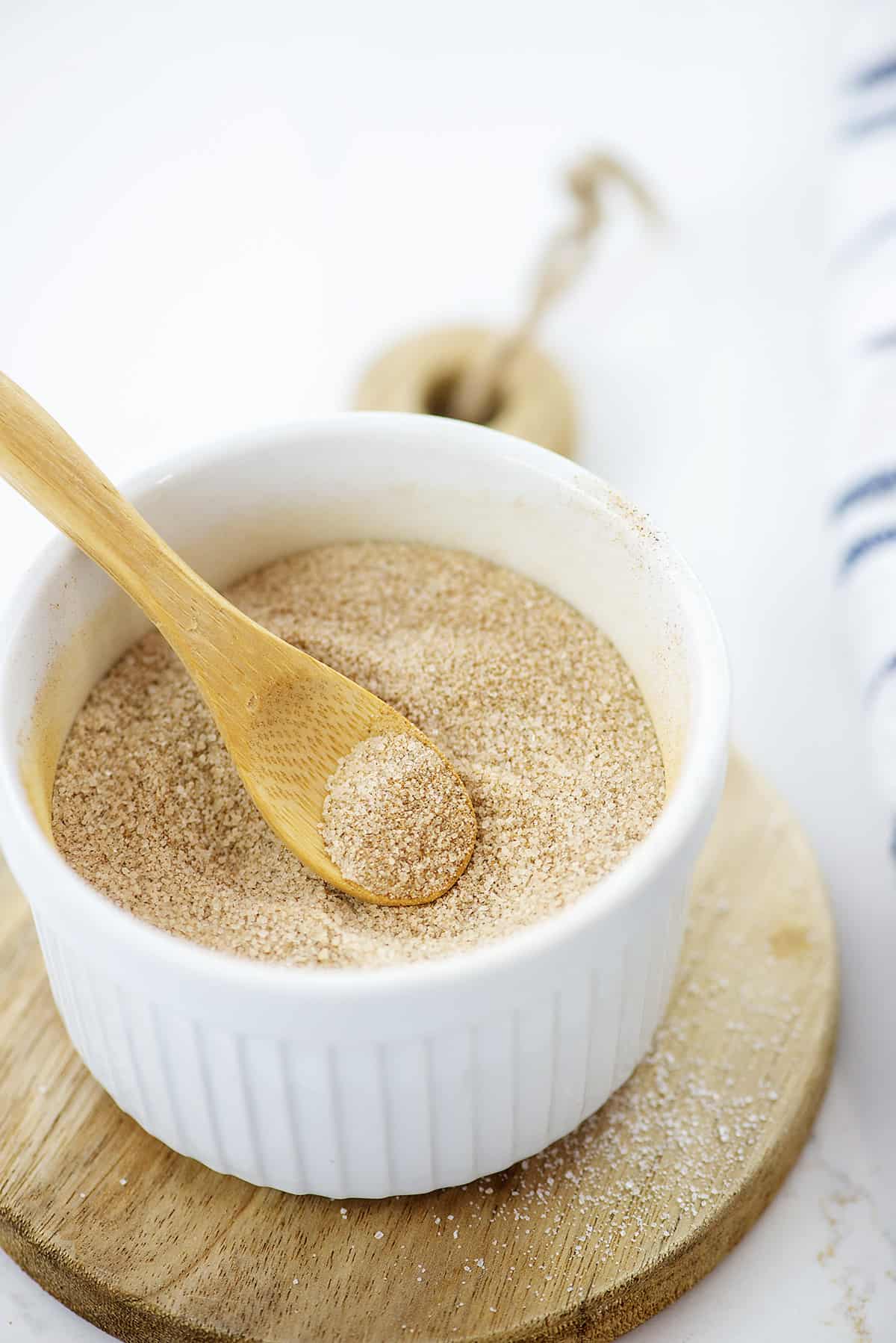 Cinnamon sugar in white bowl with wooden spoon.