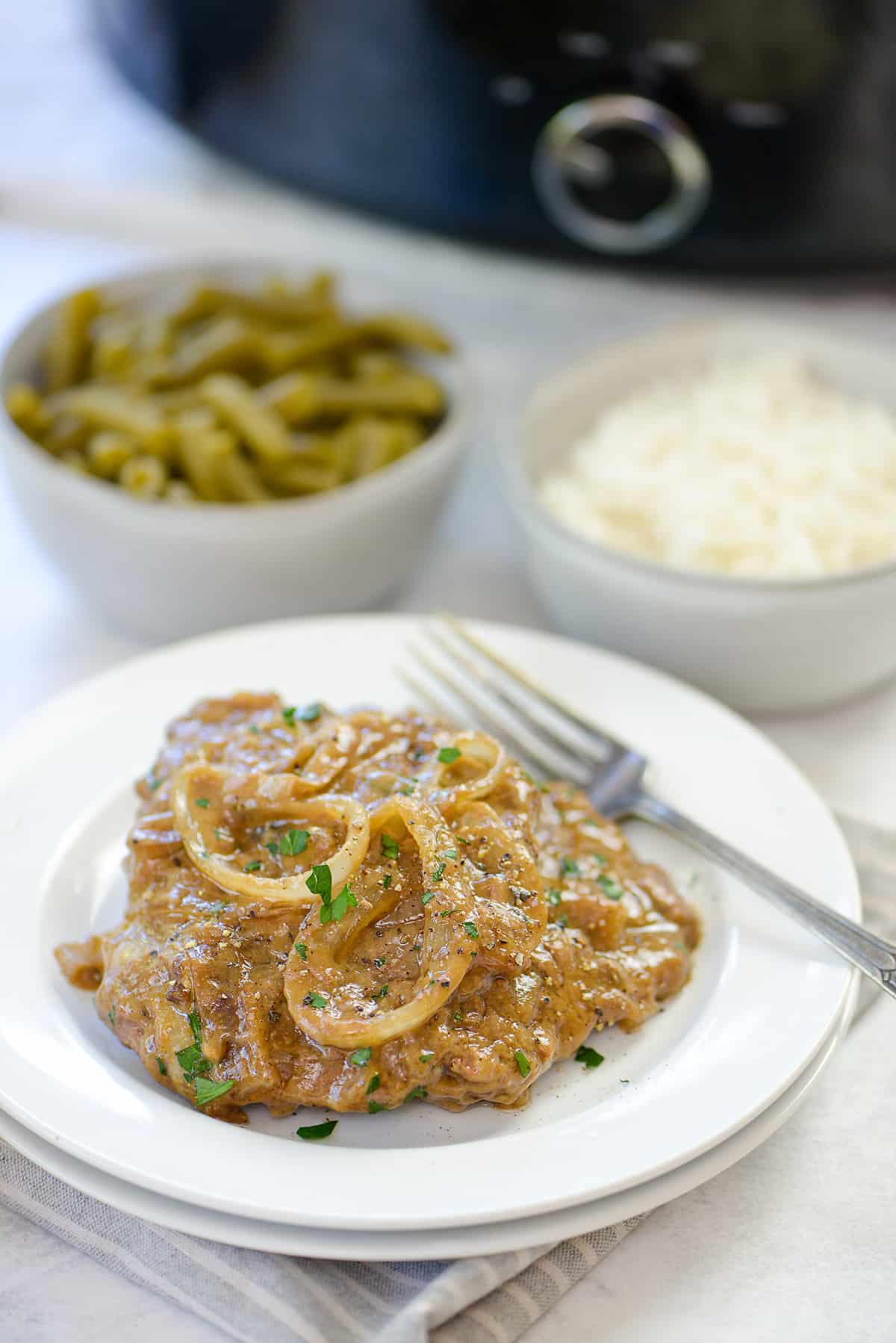 Cube steak on white plate surrounded by green beans and rice.