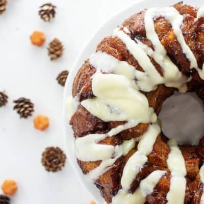 Monkey bread on white cake plate surrounded by pinecones and small pumpkins.